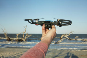 a DJI spark being held up in front of the ocean, facing the camera